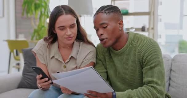 Interracial couple, phone and credit card with mortgage for ecommerce, paying bills or expenses on sofa at home. Happy man and woman with financial paperwork and smartphone app for online transaction. - Metraje, vídeo