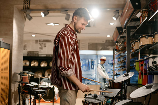 Young man buyer choosing drums at modern music shop store. Lots of music instrument in the store - Fotoğraf, Görsel