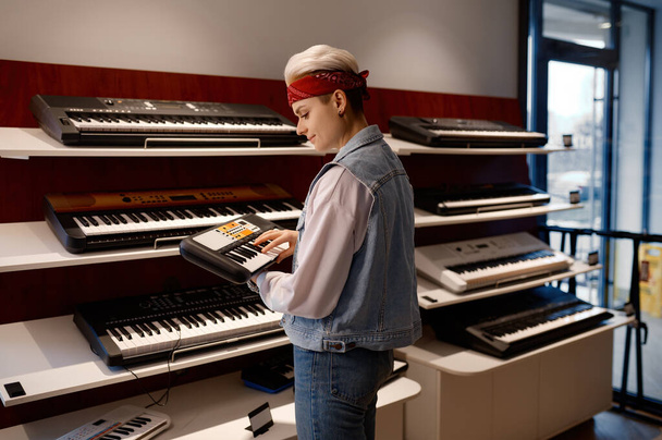 Young hipster woman holding and playing electronic mini piano at music shop store. Purchase at musical workshop sound studio concept - Fotografie, Obrázek