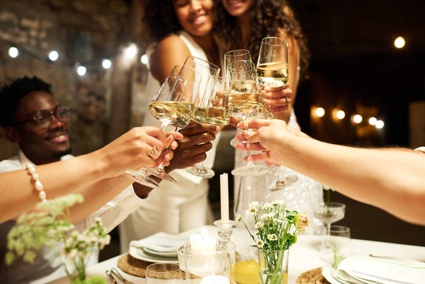 Hands of wedding guests and two intercultural brides clinking with flutes of champagne over festive table while enjoying party - Foto, imagen