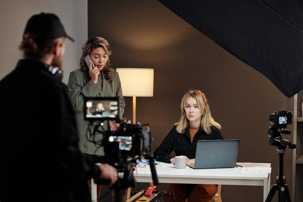 Zwei junge interkulturelle Models mit mobilen Geräten während eines Werbespots, der von einem Videofilmer mit Steadicam aufgenommen wurde - Foto, Bild