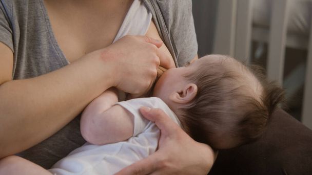 Close up shot of mother breastfeeding newborn. Woman holds baby on arms while feeding him, puts to sleep. Little child sucks breast milk from mother. Concept of childhood, motherhood, love and family. - Photo, Image