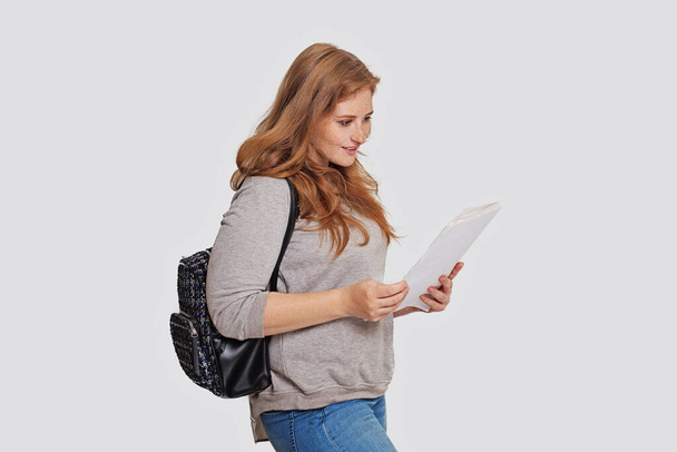 Χαριτωμένη φοιτήτρια με σακίδιο και σημειώσεις διάλεξη χαρτί κατά λευκό φόντο banner στούντιο - Φωτογραφία, εικόνα