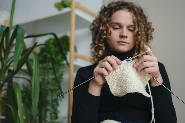 Curly haired woman sitting at home knitting and needleworking for mental health. Knitted, eco friendly knitting. Creative design. Home comfort. - Foto, Bild