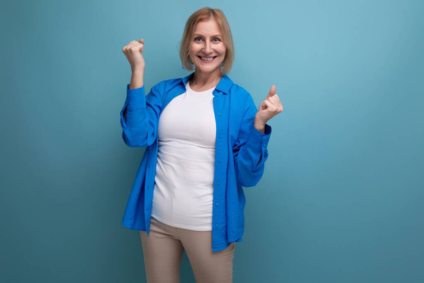πορτρέτο της θετικής ξανθιάς 60s γυναίκα σε μπλε κομψό πουκάμισο στο φόντο στούντιο. - Φωτογραφία, εικόνα