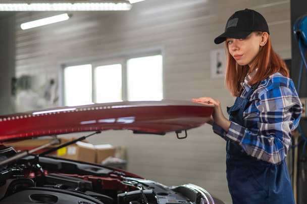 Woman auto mechanic opens the hood of a car in a car service - Фото, изображение