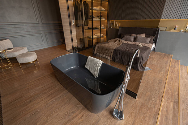 bedroom and freestanding bath behind a glass partition in a chic expensive interior of a luxury home with a dark modern design with wood trim and led light - Foto, imagen