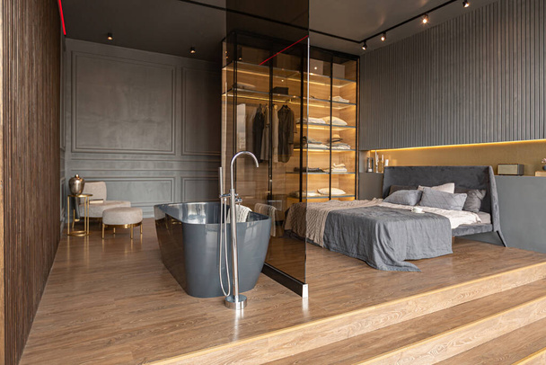 outstanding bath and bedroom of a chic modern design of a dark expensive interior of a luxurious country house with huge panoramic windows and a magnificent view of the divine forest - Photo, Image