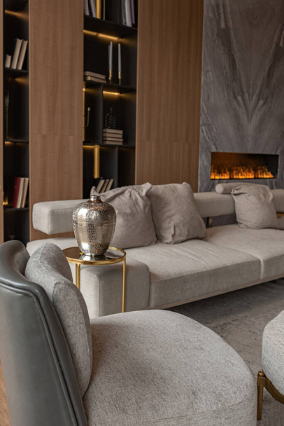 living room, marble wall fireplace and stylish bookcase in chic expensive interior of luxury country house with a modern design with wood and led light, gray furniture with gold elements - Foto, Bild