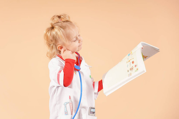 A little girl with a stethoscope holds a book in her hands and looks into it. - Photo, Image
