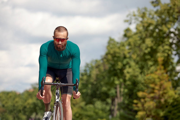 Homme fort cycliste en vêtements de sport, lunettes et casque de protection marchant avec son vélo dans la forêt pour faire une pause après avoir roulé. Bleu ciel en arrière-plan - Photo, image