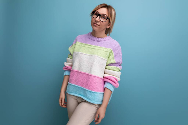 foto de cerca de una mujer rubia europea en un suéter a rayas con gafas sobre un fondo azul con espacio para copiar. - Foto, Imagen
