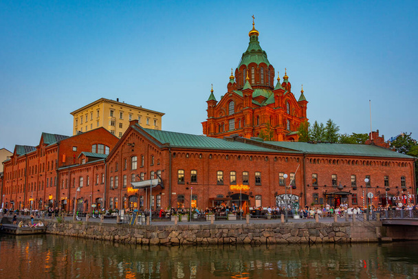 Helsinki, Finland, July 20, 2022: Sunset view of Uspenski Cathedral rising above red brick buildings of former merchant port now transformed into public place in Helsinki, Finland . - Fotó, kép
