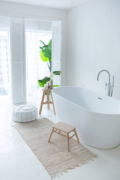 Extra white and very light minimalistic stylish elegant interior of bathroom with modern bath, green plants and wooden elements - Foto, immagini