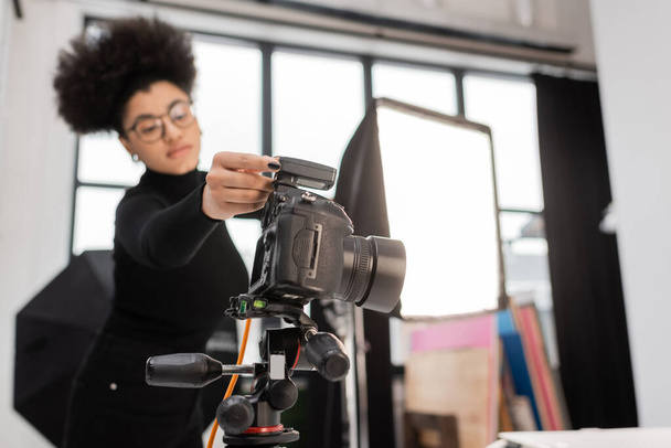 アフリカ系アメリカ人のコンテンツ制作者が写真スタジオでスポットライトの近くでデジタルカメラを調整 - 写真・画像