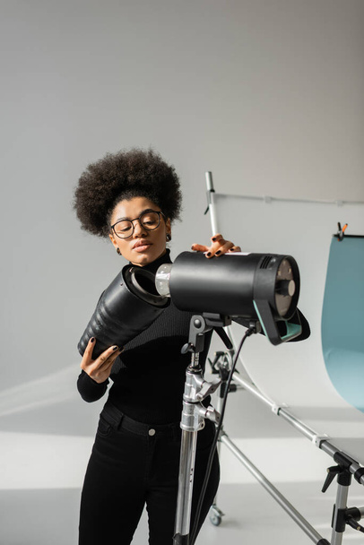 productor de contenido afroamericano en gafas que montan foco estroboscópico en estudio fotográfico - Foto, Imagen