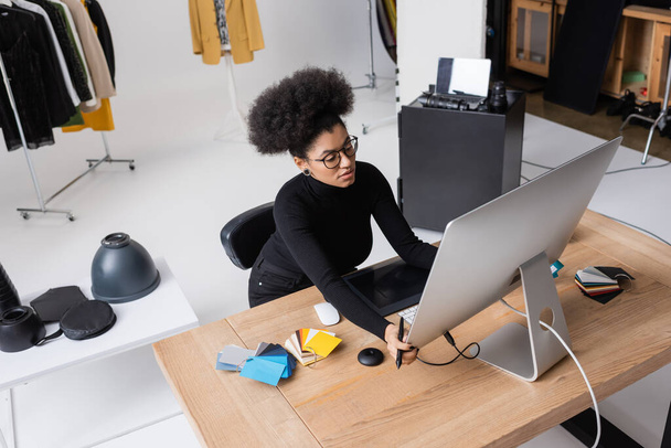 high angle view of african american retoucher adjusting computer monitor near graphic tablet and color swatches on desk in photo studio - 写真・画像