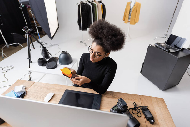 високий кут зору афроамериканського ретушера вибираючи кольори біля комп'ютера і графічного планшета в фотостудії
 - Фото, зображення