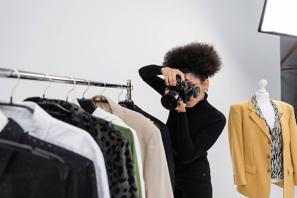 photographe afro-américain prenant des photos de la collection de vêtements à la mode sur porte-rails dans le studio photo - Photo, image
