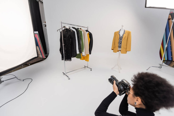 θολή αφροαμερικανός φωτογράφος που φωτογραφίζει ράγες και μανεκέν με κομψά ρούχα στο φωτογραφικό στούντιο - Φωτογραφία, εικόνα