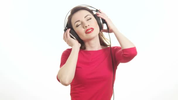 Cute woman in red listening to the music takes off big headphones and winking to the camera smiling isolated on white background medium shot - Footage, Video
