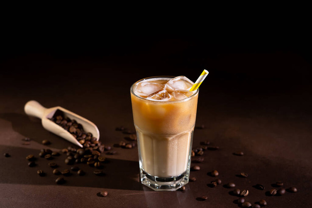 Cappuccino met ijsblokjes in een hoog glas tegen een zwarte achtergrond. IJskoffie met melk in een glas - Foto, afbeelding