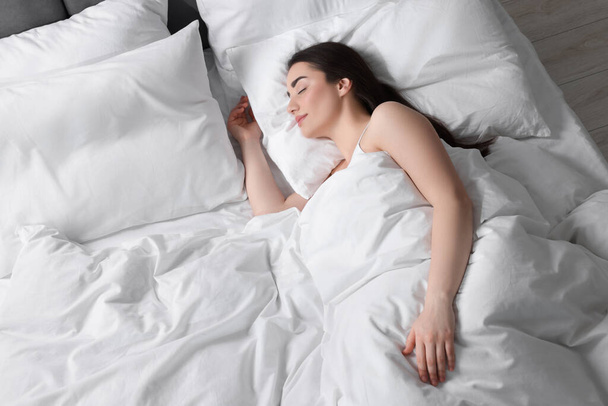 Όμορφη νεαρή γυναίκα κοιμάται σε μαλακό κρεβάτι, πάνω από την άποψη - Φωτογραφία, εικόνα