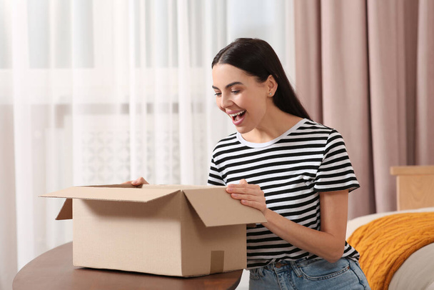 Emotional young woman opening parcel at home. Internet shopping - Fotó, kép