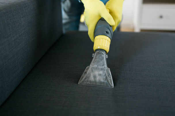 Man in protective rubber glove cleaning sofa with professionally extraction method with washing vacuum cleaner. Early spring regular cleanup. Commercial cleaning company - Foto, Imagem