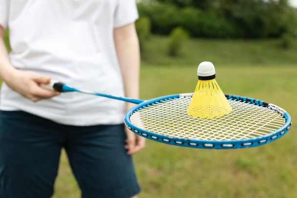 Playing badminton. A person holds a racket on which there is a shuttlecock, close-up. Park in the background. The concept of sports activity and recreation. - Photo, image