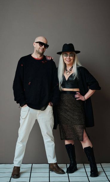 Vertical full length studio portrait of fashionable mature man and woman wearing modern goth clothes posing on camera - Fotó, kép