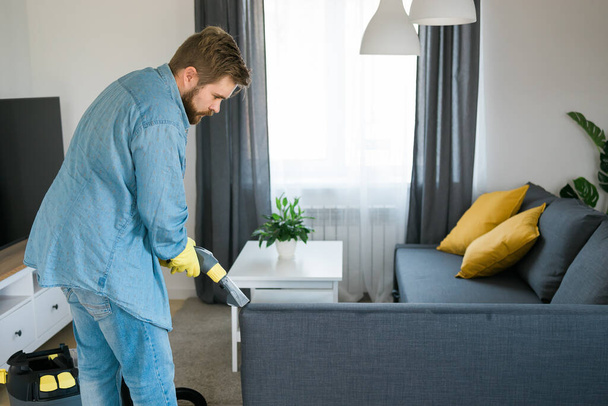 Чоловік тримає сучасний пральний пилосос і чистить брудний диван з професійним миючим засобом. Професійний весняний очищувач в домашніх умовах
 - Фото, зображення
