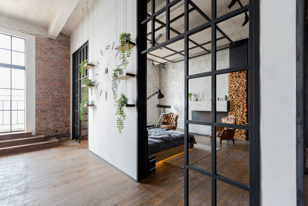 luxury studio apartment with a free layout in a loft style in dark colors. Stylish modern kitchen area with an island, cozy bedroom area with fireplace and personal gym - 写真・画像