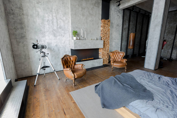 luxury studio apartment with a free layout in a loft style in dark colors. Stylish modern kitchen area with an island, cozy bedroom area with fireplace and personal gym - Фото, изображение