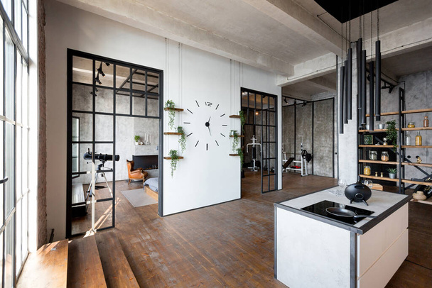 luxury studio apartment with a free layout in a loft style in dark colors. Stylish modern kitchen area with an island, cozy bedroom area with fireplace and personal gym - 写真・画像
