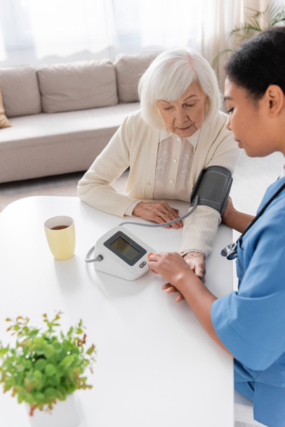 multiraciale verzorger meten van de bloeddruk van oudere vrouw met grijs haar  - Foto, afbeelding