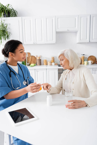 senior woman pointing with finger at pills in hands of multiracial nurse  - Foto, Imagem