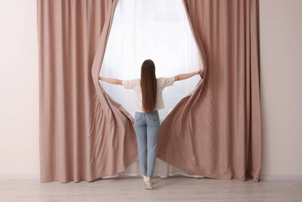 Woman opening stylish curtains at home, back view - Фото, зображення