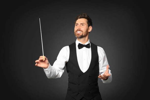 Happy professional conductor with baton on black background - Photo, Image