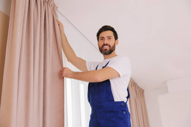 Worker in uniform hanging window curtain indoors - Фото, зображення