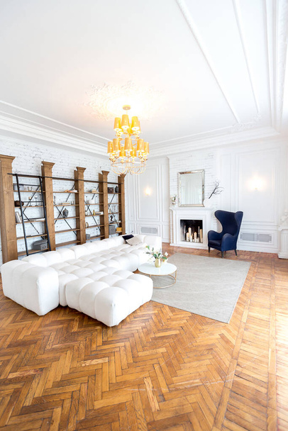 modern interior of a luxurious large bright living room. white expensive sofa and wooden shelving, white walls with moldings and a luxurious chandelier - Φωτογραφία, εικόνα