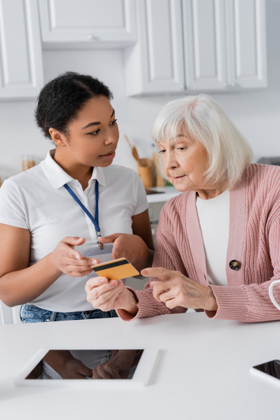 barna multiraciális szociális munkás kezében hitelkártya közelében idősebb nő otthon - Fotó, kép