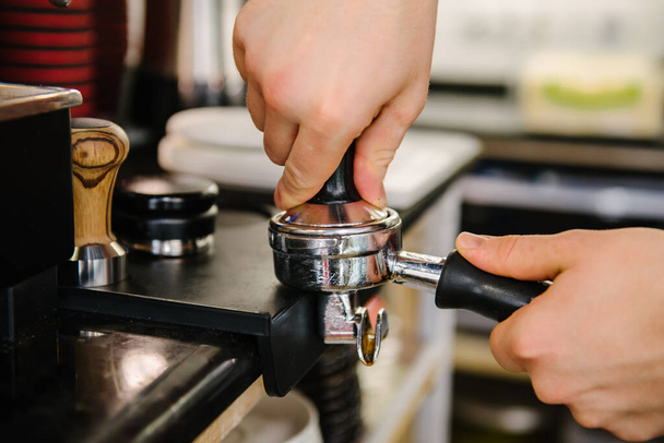 Бариста в кафе прижимает кофе к держателю и готовится сварить кофе.. - Фото, изображение
