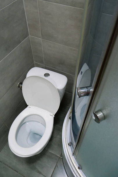 Cuarto de baño interior con inodoro blanco, cabina de ducha y azulejos grises - Foto, Imagen