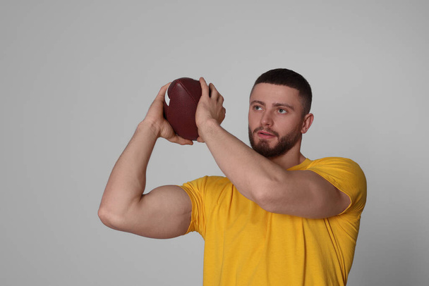Athletic young man with American football ball on light grey background - Fotografie, Obrázek