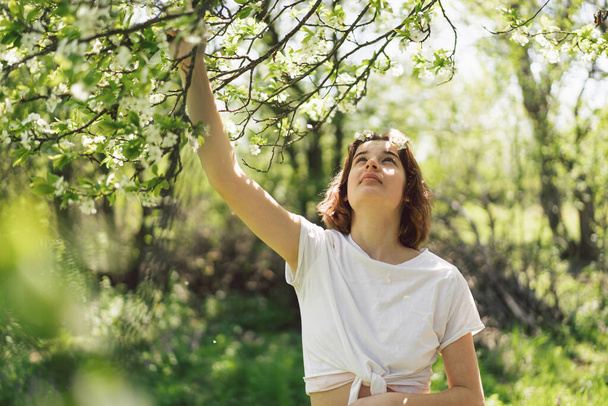 Gyönyörű tinédzser lány tavaszi virágokkal élvezi a természetet és nevet a tavaszi kertben. Egy cseresznyefa ágát tartó lány. Szabadság és boldogság koncepció. Tavasz. - Fotó, kép