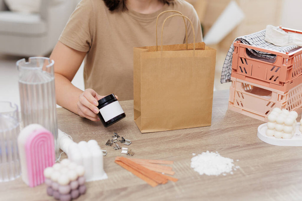 Woman packing homemade candle into paper bag sits by the table - Фото, зображення