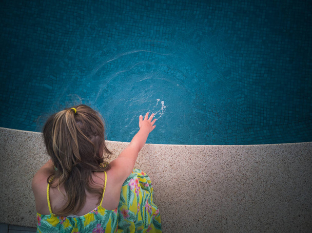 Pieni tyttö tarkistaa veden kunnon ennen uima-altaassa uimista.. - Valokuva, kuva