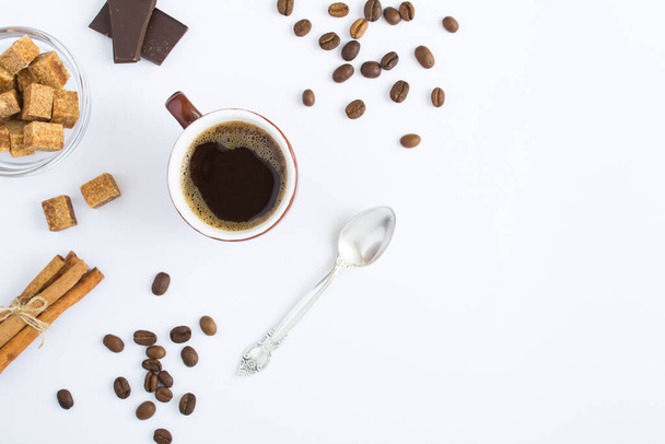 Schwarzer Kaffee in der braunen Tasse, Kaffeebohnen, Zucker und Zimt auf weißem Hintergrund. Ansicht von oben. Kopierraum. - Foto, Bild