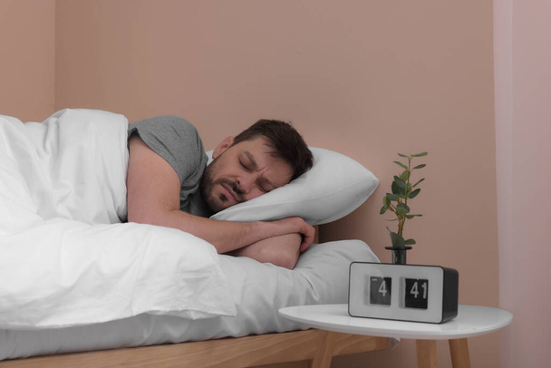 Man sleeping in bed and alarm clock on nightstand at home - Фото, зображення